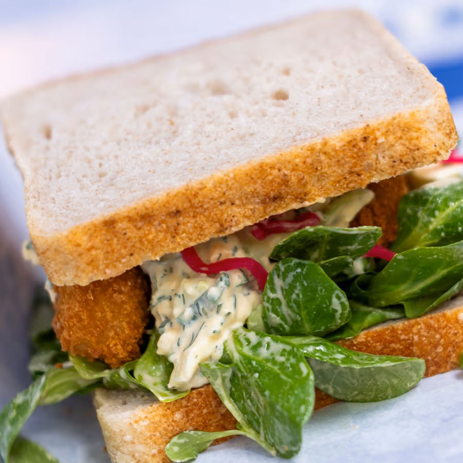 Weißbrot-Sandwich mit paniertem Belag, Salat und Kräutersauce