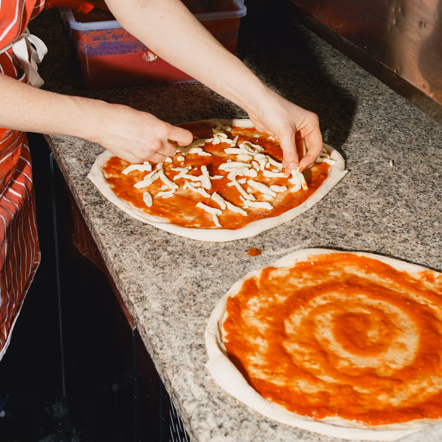 Hände belegen vorbereitete Pizzateige mit Tomatensauce und Käse