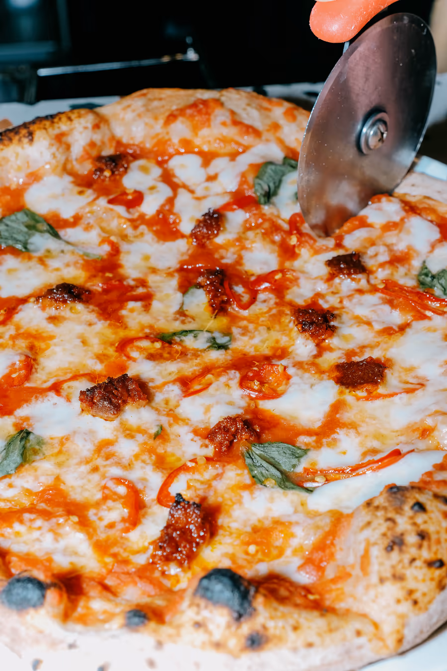 Pizzaschneider schneidet eine Pizza mit Mozzarella, Basilikum und würzigem Belag
